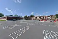 A schoolyard with various recess activities next to small playgrounds (in the distance)