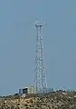 2/8 The same communication tower (man_made=tower and tower:type=communication) seen from the ground, with the antenna and a small building surrounded by a fence at the top of the mountain near the town of Hamhung.