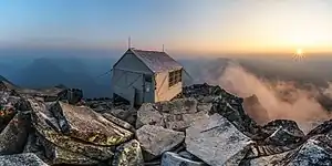 A one-room wooden structure anchored to the mountaintop by tie-down cables.
