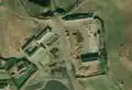 5/6 Farmyard (landuse=farmyard) composed of long buildings, surrounded by a fence dotted with hay stacks, close to a road (Maxar satellite imagery).