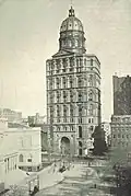 Drawing of 20-story building with a tan exterior; the roof is topped with a large, gold dome and a flagpole.