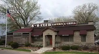 A one-story stone building with burgundy awnings and a sign announcing 5-8 Club Tavern & Grill