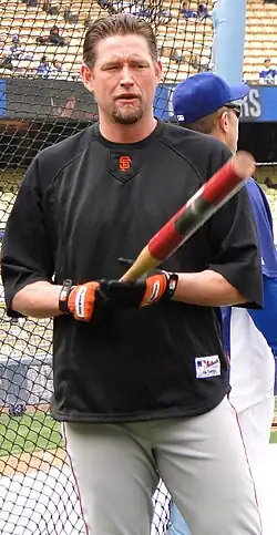 A man in a black baseball uniform pointing a bat towards the camers