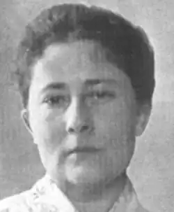 A white woman with dark hair dressed simply, back from her face and up from her neck and shoulders.