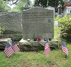 Large gravestone. On the mantle of the grave is four hockey pucks and a rose between them. Four small American flags are in the ground in front of the grave as well