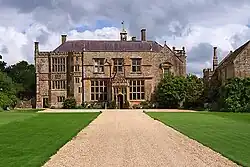 Yellow stone building at the end of a driveway accessed via stone gateposts