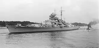 Black and white photograph of the port side of a Bismarck class battleship in a body of water.