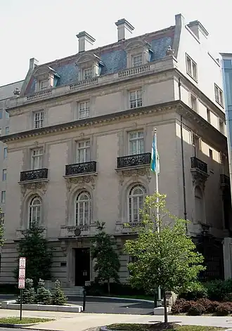 Four storey yellow brick building with Roman arch windows and mansard roof, with green and white flag on flagpole