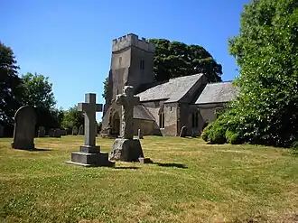Stone building with square tower. In the foreground are stone crosses, gravestones and trees.