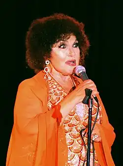 A woman wearing an orange dress and earrings, holding a microphone