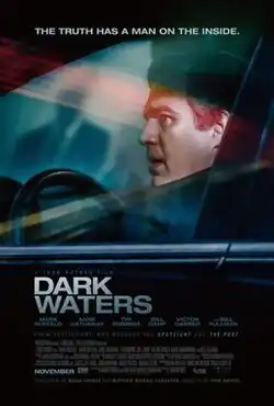A man sitting behind the wheel of a car, a vague figure in a suit, is reflected in the window glass.