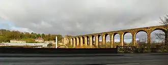 A curving stone viaduct bathed in sunshine on the right of the image; houses and a small valley are shown on the left