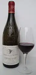 A glass of red wine next to a dark green bottle with French text on the label
