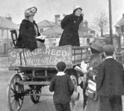 Two women giving speeches from a cart to a small crowd