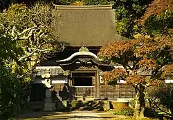 A wooden building behind a roofed wall with a small Chinese style gate.