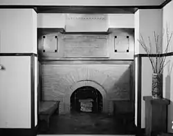 An inglenook at the center of the living room, with a round-arched brick fireplace. There is a mirror above the mantel.