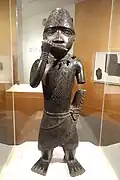 Figure of a horn blower; 1504–1550; copper alloy; 62.2 x 21.6 x 15.2&nbsp;cm (241⁄2 x 81⁄2 x 6 in.); Brooklyn Museum (New York City). Blowing a horn or flute with his right hand, his left arm is truncated. He also wears a netted cap with chevron design decorated with a feather.