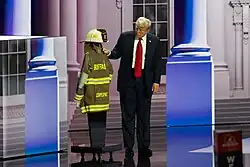 Donald Trump, who survived an attempted assassination in Pennsylvania in July 2024. This image shows Donald Trump paying respect to Corey Comperatore's firefighter uniform; he lost his life in the assassination attempt.