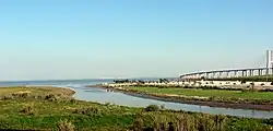 a tall long bridge in the background, with a park and river in the foreground
