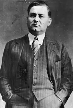 Moran standing, wearing a suit and looking at the camera