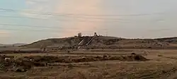 A general view of the diversion HPP. Two massive white penstocks run down from the top of an arid hill to its base. A water intake structure is located at the top.