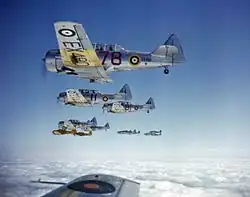 Silver fighter aircraft, marked with the British Royal Air Force's distinctive roundel, flying above the clouds in formation