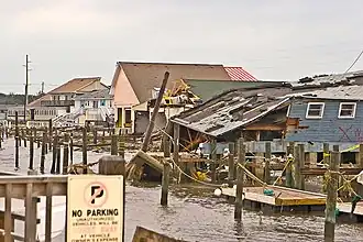 An image of multiple damaged buildings along a dock; one has collapsed on itself.
