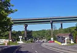 A pair of bridges pass from left to right on tall supports that tower over the other structures in the area, such as telephone poles and single-story buildings. The two-lane NY 22 passes underneath the bridge and proceeds into the background.