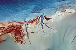 Orange islands cut by deep blue channels ending in blue ocean in the upper part of the image and beginning in a whiter lagoon in the lower part of the image