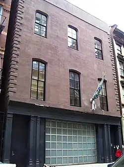 A three-story brick building whose lowest floor is painted black with a large frosted glass and silver metal window taking up most of the street frontage.