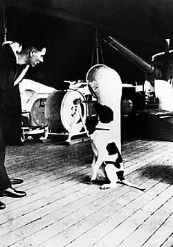 A dog sitting on the deck of a ship, being spoken to by a man in a military uniform