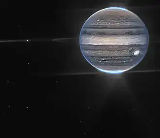 Image of Jupiter showing its faint rings, two small moons, auroras, and atmospheric features.