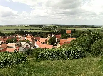 Low hills, barely higher than the church's steeple, surround a village.