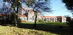 Arts and crafts style hospital building in red sandstone with red tiled roof, set in landscaped grounds. The central block has three storeys, with long one-storey wings stretching out on either side.