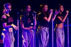 Little Mix performing in baggy jeans and black crop tops on stage.