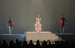 A color photograph of Marina performing live with backup singers while flowing their arms.