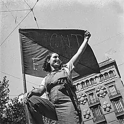 Militiawoman standing on a barricade holding an anarchist flag