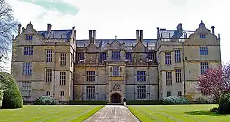 Facade of house built of yellow stone. Three floors with many large, mullioned windows and Dutch gables to the roof.