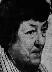 An older white woman with dark hair, wearing a plaid collared shirt.