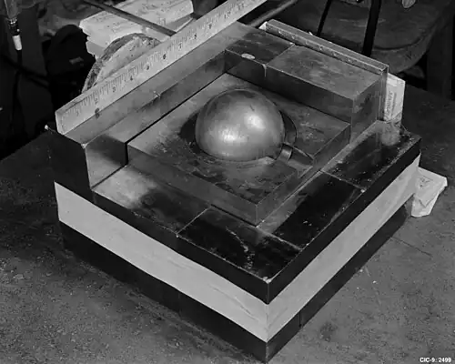 A square base of metal blocks, with a smaller square of metal on the top in the center, a Cooper block (the "core") contained in its center. A ruler along one side of the base shows roughly 10.5 inches (270 mm) square.