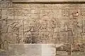King Taharqa and the gods of Thebes. Standing on the left, he offers "a white loaf" to his father Amun-Re, who is accompanied by Mut, Khonsu and Montu, Kawa shrine.[63]