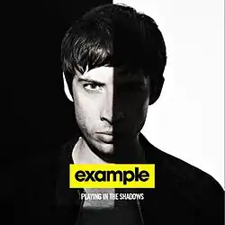 A photo of Example, with a shadow covering the right side of him. The artist's name is seen in black underneath.