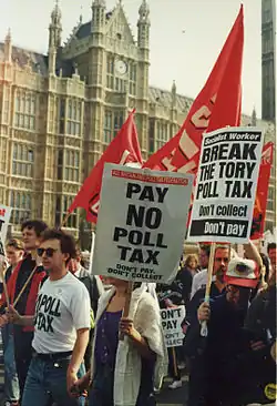 Protesters marching in front of the Palace of Westminster carrying red banners and placards with anti-poll tax slogans: "Don't Pay – Don't Collect"