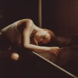 A sepia-toned photograph of Lenae leaning over to wash her hair in a grungy tub as water comes out a pipe.