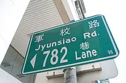 A green street sign for 軍校路, romanized as Jyunsiao Rd.