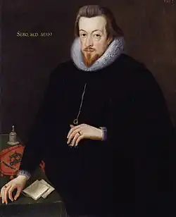A three-quarter portrait of a white man, dressed entirely in black with a white lace ruff. He has brown hair, a short beard, and a neutral expression. His left hand cradles a necklace he is wearing. His right hand rests on the corner of a desk, upon which are notes, a bell, and a cloth carrying a crest. Latin text on the painting reads "Sero, Sed, Serio".