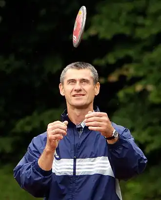 Romas Ubartas, pictured from about the stomach up, tossing a discus up in the air above his head and looking up at it.