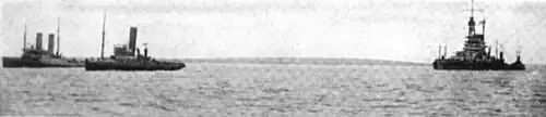 Two small boats pull a larger vessel through calm waters.
