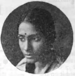 A young South Asian woman, dark hair parted center and dressed to the nape, in a circle frame