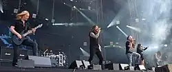 Amaranthe performing on stage. All six band members can be seen.